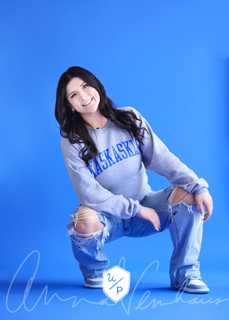 senior girl in a college sweatshirt against a blue background