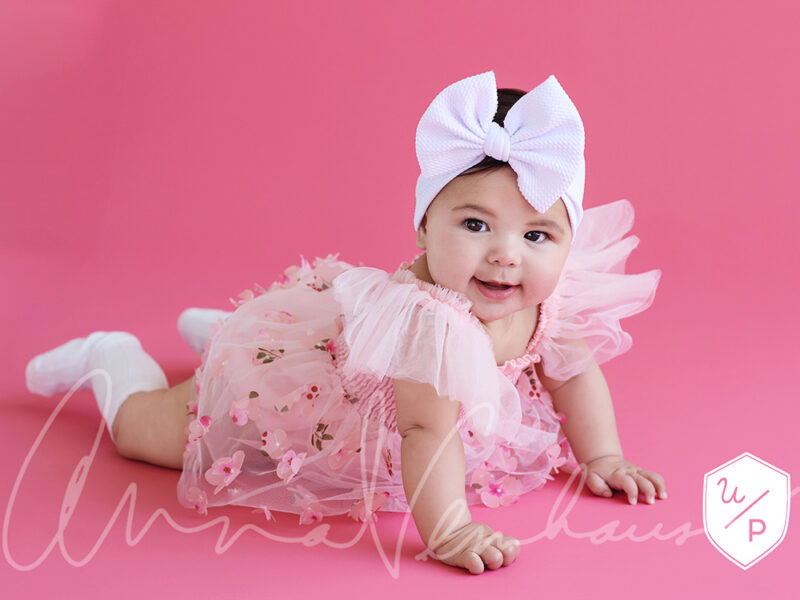 6mo old girl in frilly dress and bow against a hot pink background