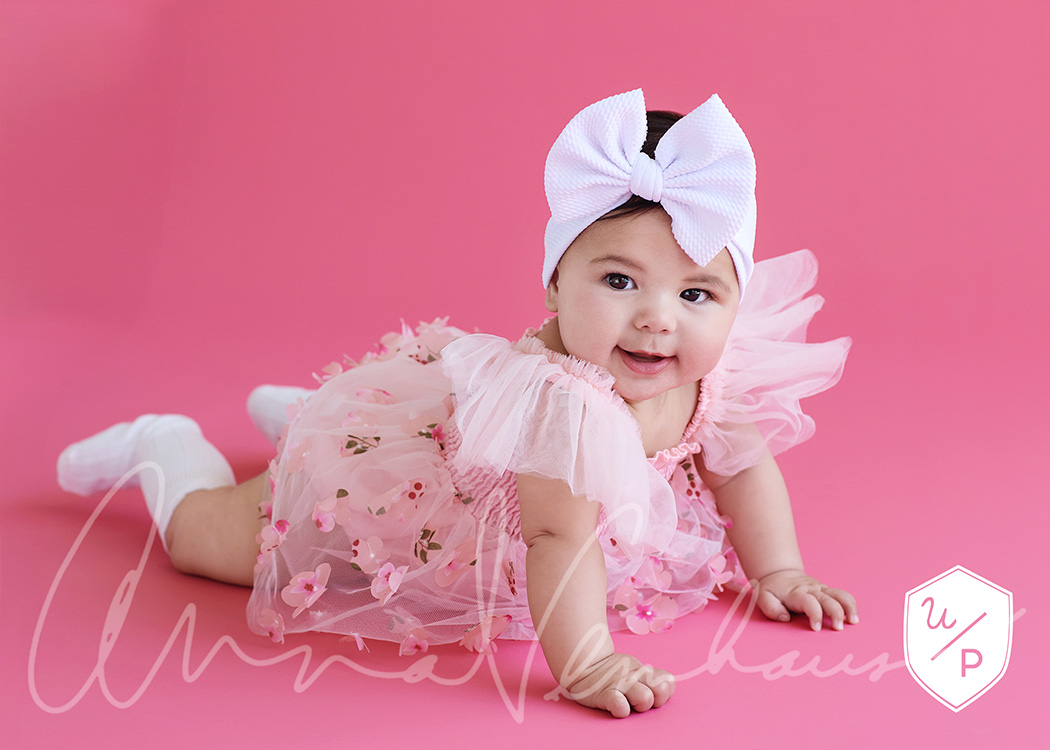 6mo old girl in frilly dress and bow against a hot pink background