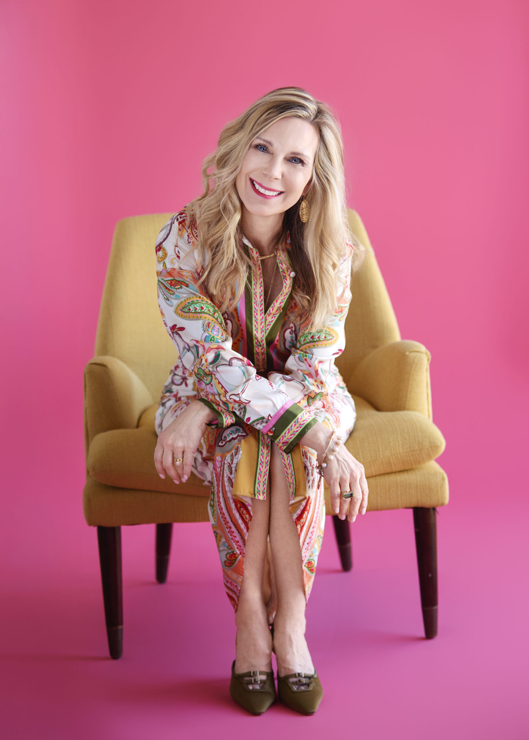 woman in bold dress on yellow chair against pink background
