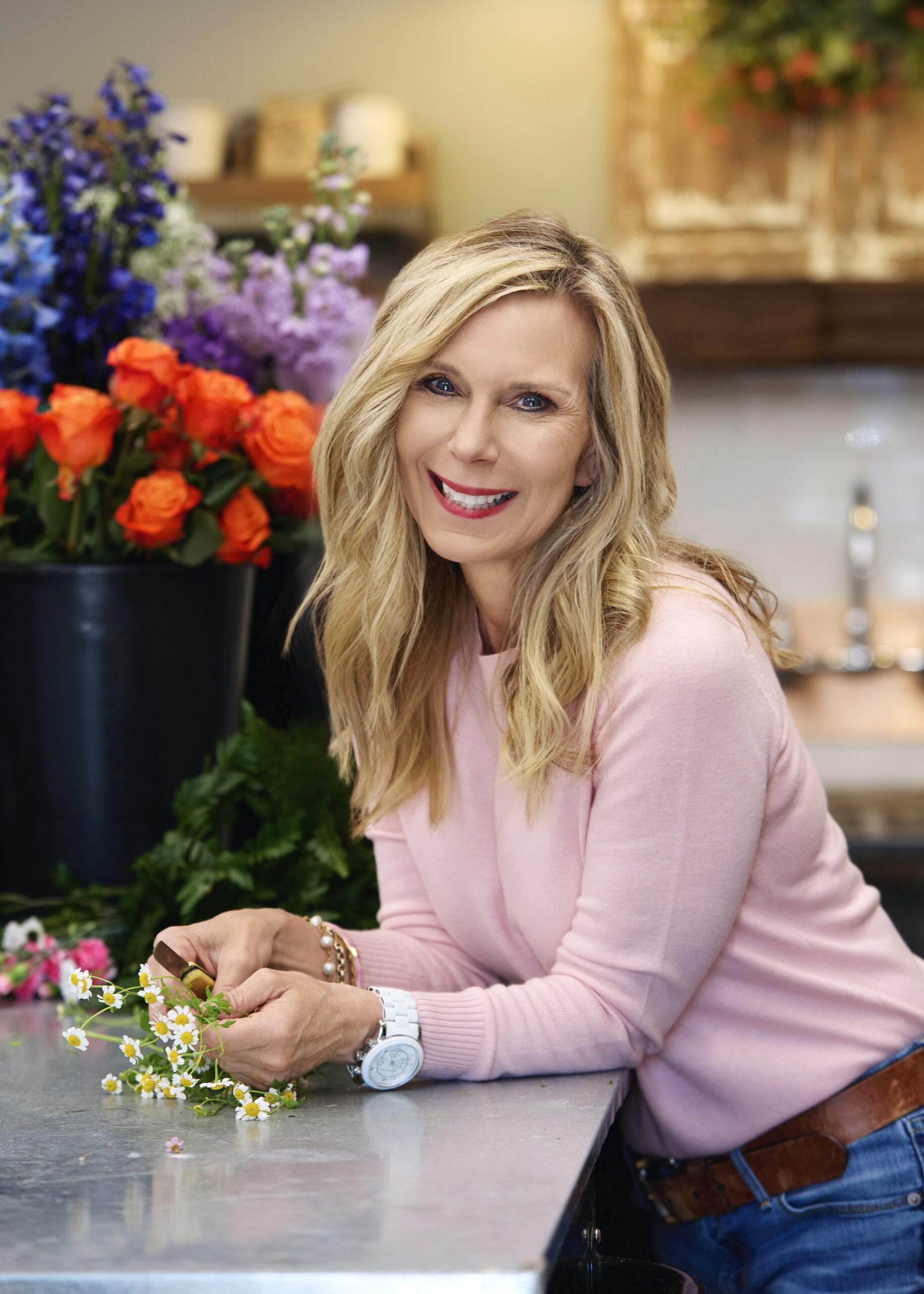 woman in pink sweater leaning on counter with flowers in the background