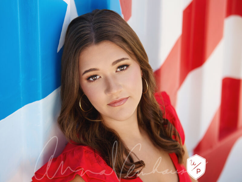 brunette senior girl wearing red posed in front of American flag mural