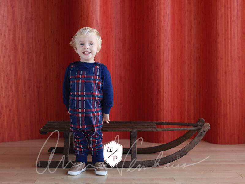 blonde boy in plaid outfit in front of vintage wooden sled