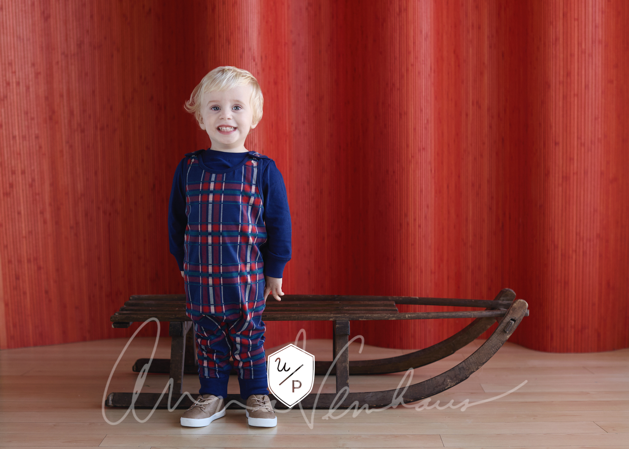 blonde boy in plaid outfit in front of vintage wooden sled